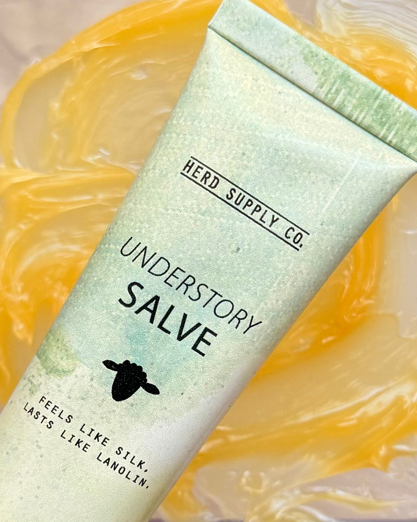 Understory Salve lanolin balm tube on a golden textured surface, part of preorder bundle