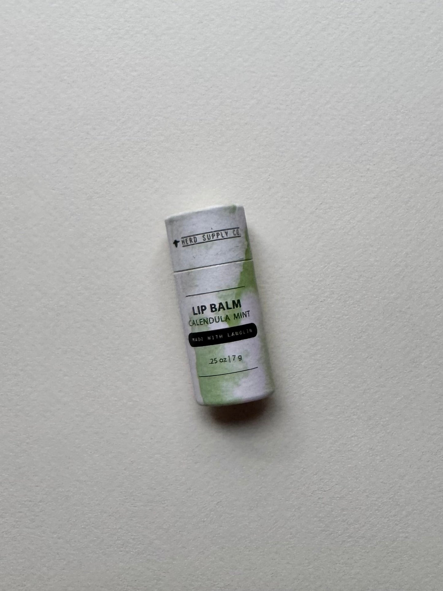 Calendula Mint Lip Balm tube in cardboard packaging on a light gray surface